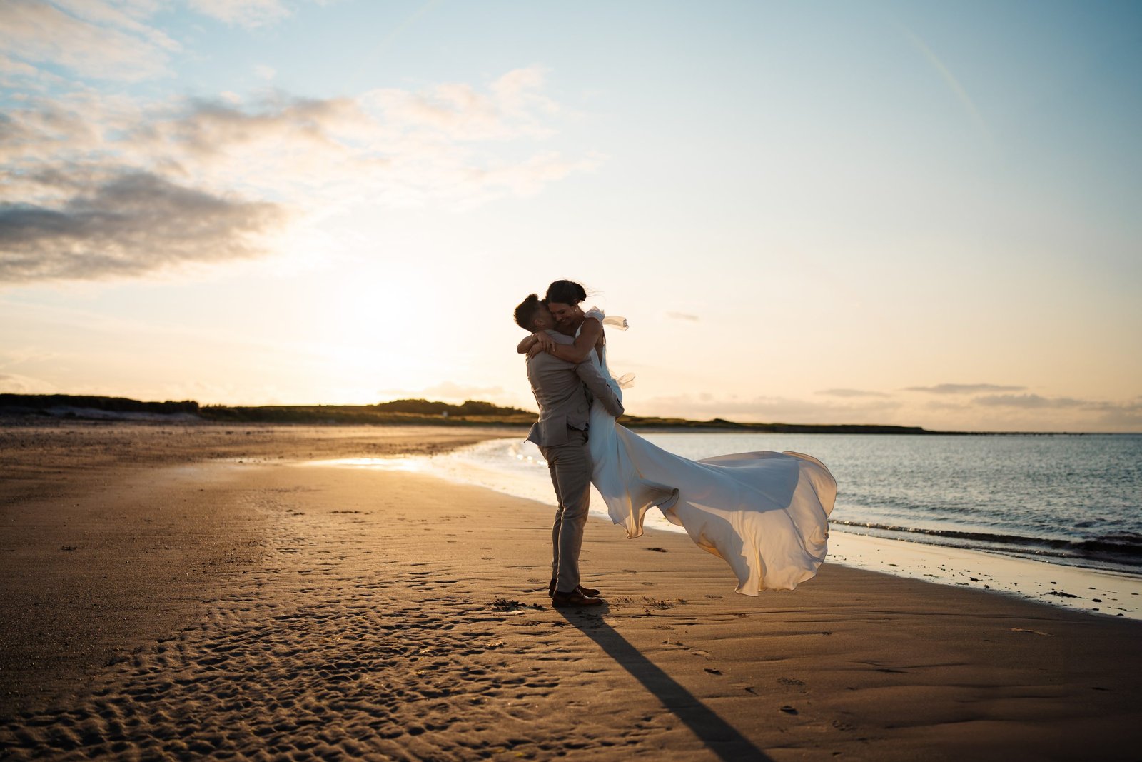 bride and groom spin around on a beach at sunset